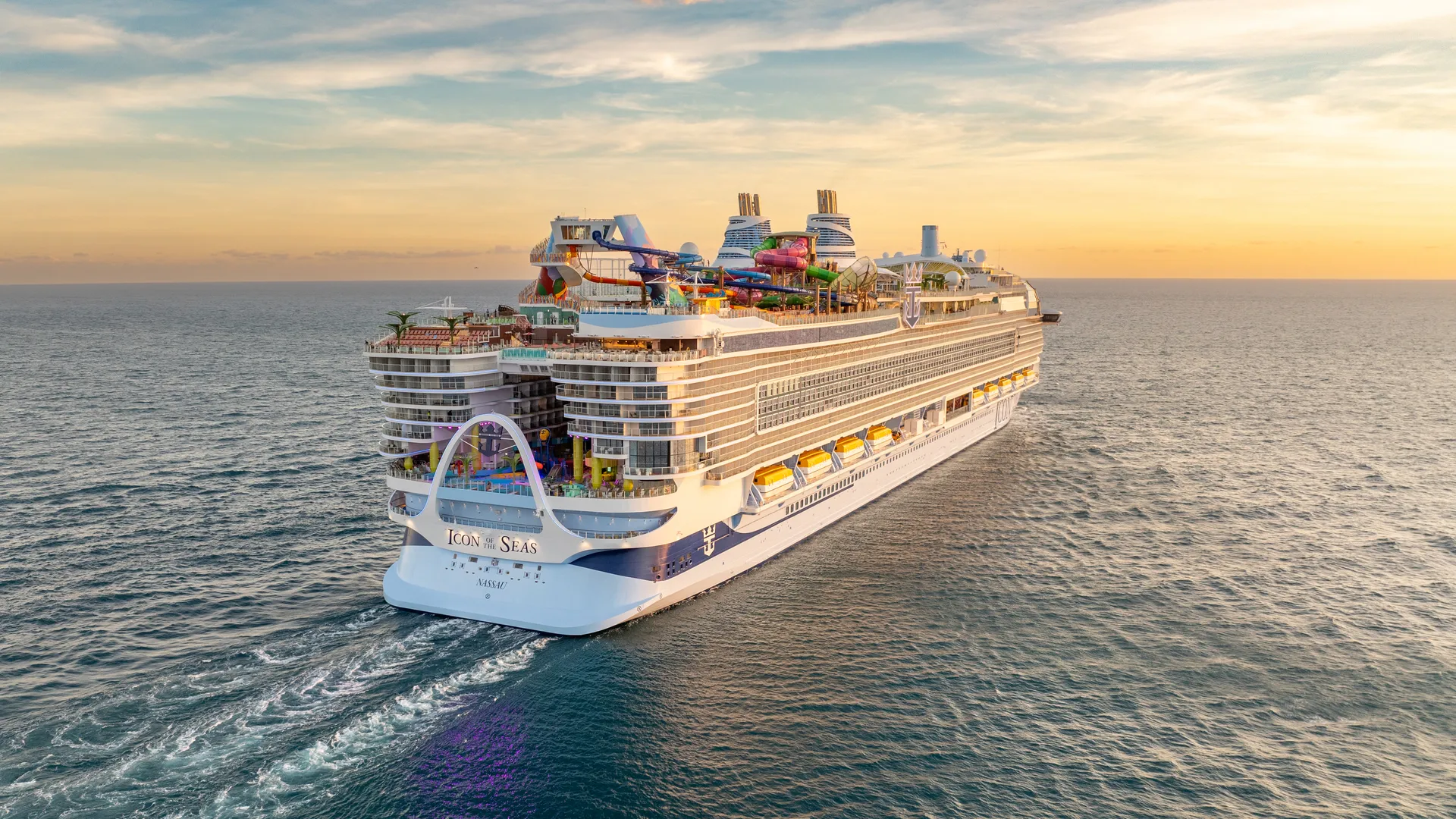 Die Icon of the Seas fährt bei Sonnenuntergang auf dem Meer. Von hinten gesehen, zeigt sie bunte Wasserrutschen und Freizeitbereiche. Eine klare Welle ist erkennbar.