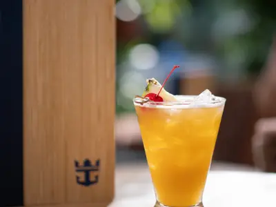 Tropischer Cocktail mit Ananas und Kirsche, Eiswürfeln in einem Glas. Links ein Royal Caribbean Logo auf Holz, aufgenommen an Bord der Icon of the Seas.