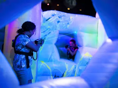 Zwei Personen spielen Laser Tag in einer blauen, aufblasbaren Arena auf der Icon of the Seas. Ein grüner Laserstrahl ist zu sehen.