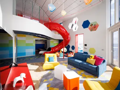 Ein farbenfroher Spielbereich auf der Icon of the Seas. Eine große rote Rutsche verbindet die beiden Ebenen. Der Raum hat bunte Wände, helle Möbel und große Fenster mit Blick auf das Meer.