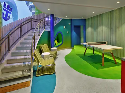 Ein lebhafter Freizeitbereich auf der Icon of the Seas mit einer geschwungenen Treppe, farbenfrohen Sitzgelegenheiten, einer gemütlichen Nische und einem modernen Ping-Pong-Tisch auf einem grünen Boden.