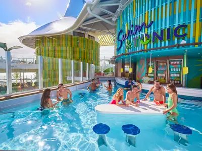 Ein sonniger Poolbereich an Bord der Icon of the Seas zeigt mehrere Gäste, die im Wasser an einer Swim-up-Bar mit dem Schriftzug 'Swim & Tonic' Getränke genießen. Die Umgebung ist farbenfroh gestaltet.