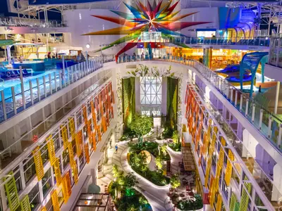 Atrium der Icon of the Seas mit zentralem Garten, bunten Balkonen, Poolbereich und farbenfrohem Sternendach bei Nacht.