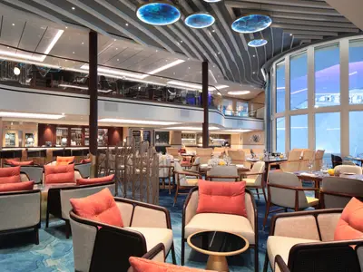 Innenansicht der Icon of the Seas: Ein zweistöckiger Bereich mit Bar, Lounge, Restaurant, großen Panoramafenstern und einer künstlerischen Deckengestaltung mit Leuchten.