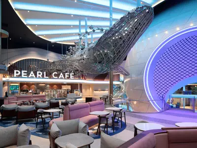 Blick ins Pearl Café der Icon of the Seas mit einer großen, metallenen Wal-Skulptur und modernen Sitzbereichen. Im Hintergrund ein leuchtender Torbogen.
