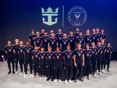 Die Fussballmannschaft Inter Miami CF posiert in schwarzen Trikots mit pinken Akzenten und Logos von Royal Caribbean vor einer beleuchteten Wand mit Vereins- und Reedereilogo.