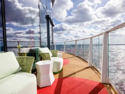 Moderne Außenterrasse der Icon of the Seas mit Lounge-Möbeln, Glasgeländer und weitem Meerblick unter bewölktem Himmel.