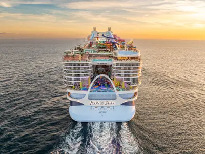 Heckansicht der Icon of the Seas bei Sonnenuntergang auf dem Meer. Bunte Wasserrutschen, Pools, Balkonkabinen und eine Kielwelle prägen das Bild.