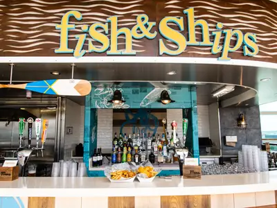 Die Fish & Ships Bar auf der Independence of the Seas. Am Tresen Zapfanlagen, Spirituosen, Fish & Chips. Maritimes Dekor, Ruder, große Fenster.