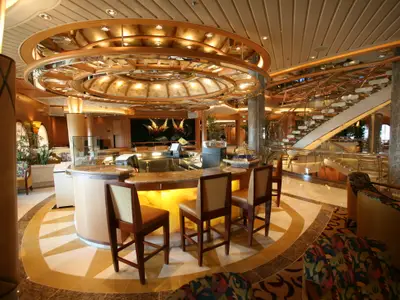Innenansicht der Independence of the Seas zeigt einen eleganten Bar- und Atriumbereich mit runder Bar, Barhockern, einer geschwungenen Treppe und dekorierter Decke.