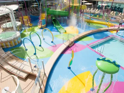 Der farbenfrohe Wasserpark H2O Zone auf der Independence of the Seas zeigt Wasserrutschen, Spritzdüsen, Pools und Whirlpools. Ein Kind und ein Erwachsener sind erkennbar.