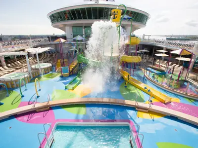 Der farbenfrohe Wasserspielplatz der Independence of the Seas mit Rutschen und Kippeimer. Ein Pool und Liegeflächen sind sichtbar.