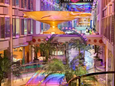 Die Royal Promenade auf der Independence of the Seas, mit goldener Skulptur, Palmen und lebendiger Beleuchtung. Mehrere Ebenen, Kabinenbalkone und eine Kuh-Statue sind sichtbar.
