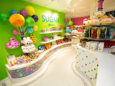 Bunter Süßigkeitenladen 'Sugar Beach' auf der Independence of the Seas. Regale mit Süßigkeiten, Plüschtieren und eine Auslage mit vielen bunten Kugeln sind sichtbar.