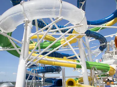 Bunte Wasserrutschen in Blau, Gelb, Grün und Transparent auf der Independence of the Seas. Weiße Stützstrukturen halten die verschlungenen Röhren vor blauem Himmel. Wasser ist sichtbar.
