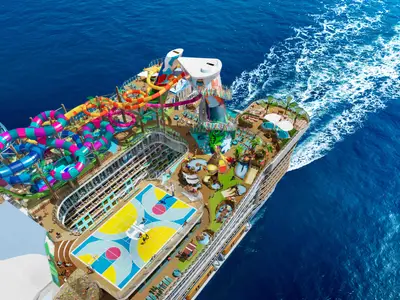 Luftaufnahme der Legend of the Seas von Royal Caribbean International. Das Schiff fährt auf blauem Wasser und zeigt auf dem Oberdeck bunte Wasserrutschen, einen Sportplatz und mehrere Pools.