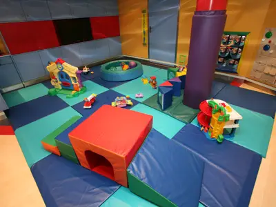 Bunter Indoor-Spielbereich auf der Liberty of the Seas mit Matten, Spielhaus, Bausteinen, Bällebad und Rutsche. Wände farbig, gepolsterte Säule.