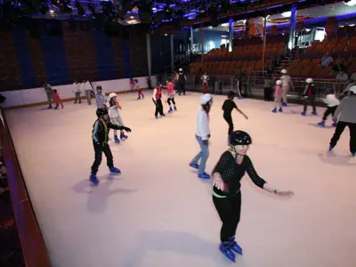 Innenansicht der Eisbahn auf der Liberty of the Seas, mit mehreren Schlittschuhläufern. Einige tragen Helme; Tribünen und Zuschauer sind im Hintergrund zu sehen.