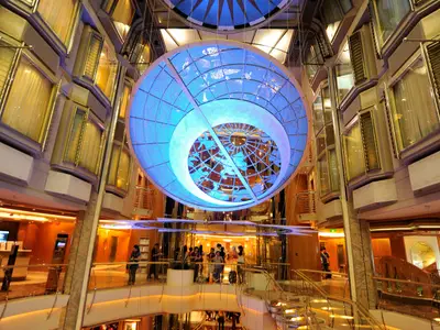Atrium der Mariner of the Seas: Eine imposante, blau leuchtende Hängekugel mit Himmelsdarstellung überblickt mehrere Decks mit Kabinen und Passagieren.