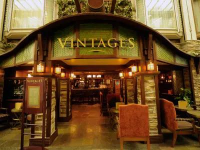 Die Vintages Bar auf der Mariner of the Seas, mit rustikalem Interieur aus Stein und Holz. Der Eingangsbereich zeigt eine Bar, Tische und Stühle, alles warm beleuchtet.