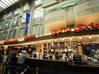 Blick in die Royal Promenade der Mariner of the Seas mit Cafés, einer Ben & Jerry's Eisdiele und Gästen. Darüber simulierte Kabinenfassaden.
