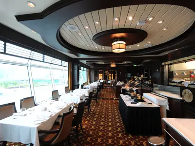 Das Hauptrestaurant auf der Mariner of the Seas: elegante Tische an großen Fenstern, kunstvolle Decke, Buffet. Dunkles Holz, gemusterter Teppich.
