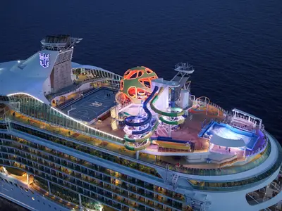 Nahaufnahme des beleuchteten Oberdecks der Mariner of the Seas bei Dämmerung, mit Basketballplatz, Wasserrutschen, Surfsimulator und dem charakteristischen Globe.