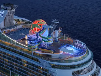 Die Mariner of the Seas bei Nacht: Beleuchtete Oberdecks mit bunten Wasserrutschen, Basketballfeld, Kletterwand und Surfsimulator sind aus der Vogelperspektive zu sehen.
