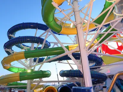 Nahaufnahme der bunten Wasserrutschen der Mariner of the Seas. Zu sehen sind mehrere blaue, grüne und gelbe Röhren, die von einem weißen Gerüst vor blauem Himmel gehalten werden.