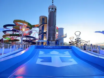 Der beleuchtete FlowRider Surfsimulator auf dem Deck der Mariner of the Seas. Im Hintergrund sind bunte Wasserrutschen und ein hoher Turm bei Dämmerung sichtbar.