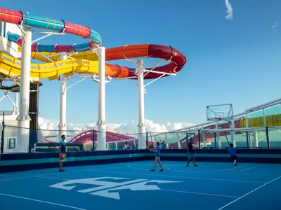 Das Oberdeck der Navigator of the Seas zeigt einen blauen Basketballplatz mit spielenden Personen und mehrere bunte Wasserrutschen unter blauem Himmel.