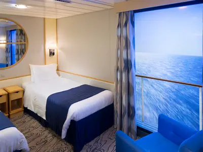 Blick in eine Innenkabine der Navigator of the Seas mit zwei Einzelbetten. Blaue Vorhänge und Sessel ergänzen die Einrichtung.