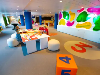 Bunter Kinderbereich auf der Navigator of the Seas. Zwei Kinder spielen an einem Puzzletisch. Die Wände sind mit leuchtenden, bunten Formen dekoriert; große Zahlen zieren den Boden.