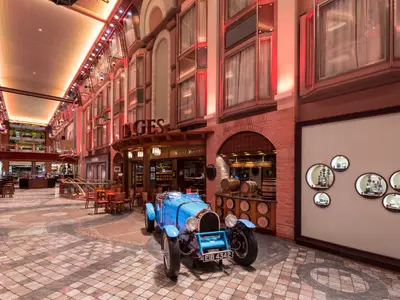 Innenaufnahme der Navigator of the Seas. Eine Promenade mit blauem Oldtimer, Geschäften und Bars. Rechts ein Weinkeller und eine Schmuckvitrinenwand.