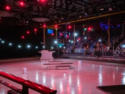 Innenansicht der Eisbahn der Navigator of the Seas mit Requisiten. Rote Bühnenbeleuchtung und Handylichter des Publikums auf den Rängen.