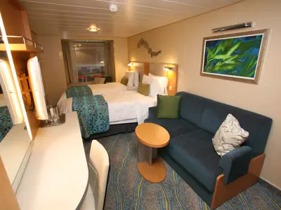 Geräumige Kabine der Oasis of the Seas mit zwei Betten, Sofa, Schreibtisch und Fenster. Moderne, helle Einrichtung mit gemustertem Teppichboden.
