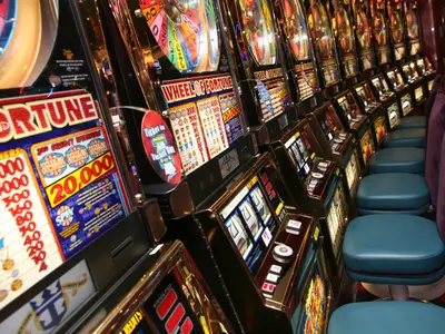 Eine lange Reihe leuchtender Spielautomaten mit Sitzen in einem Casino an Bord der Oasis of the Seas. Einige Maschinen zeigen "Wheel of Fortune"-Logos, die Bestuhlung ist dunkelblau und lila.