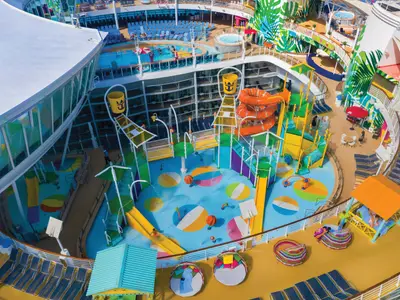 Eine Draufsicht auf den lebhaften Wasserpark der Oasis of the Seas mit bunten Rutschen, Planschbecken und Spritzdüsen. Kinder spielen im Wasserbereich. Im Hintergrund sind Pools und Liegestühle zu sehen.