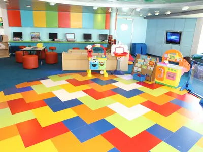 Eine helle und farbenfrohe Kinderspielzone an Bord der Oasis of the Seas, ausgestattet mit interaktiven Computern, Spielzeug und einem auffälligen, mehrfarbigen Bodenmuster.