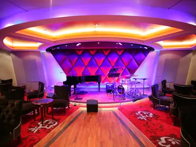 Ein luxuriöser Live-Musik-Club an Bord der Oasis of the Seas mit einer Bühne, Grand Piano und Schlagzeug. Farbige Beleuchtung und elegante Sitzmöbel prägen das stilvolle Ambiente.