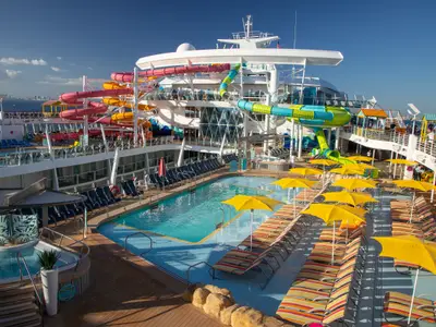 Das sonnige Pooldeck der Oasis of the Seas von oben: Bunte Wasserrutschen, Pools, Whirlpool und viele Sonnenliegen mit gelben Sonnenschirmen sind zu sehen.