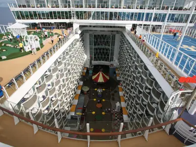 Die Oasis of the Seas von oben: Ein Minigolfplatz, ein blauer Sportplatz und ein Karussell sind im offenen Bereich zu sehen. Viele Balkonkabinen säumen die inneren Decks an den Seiten.