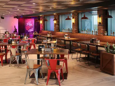 Innenansicht eines Restaurants an Bord der Oasis of the Seas. Man sieht Holztische, Stühle und eine lange braune Lederbank entlang von Ziegelwänden. Kakteen schmücken die Fensterbänke.