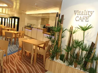 Innenansicht des Vitality Cafés auf der Oasis of the Seas. Helle Möbel, ein Buffet und eine Bambusdekoration prägen den Raum mit gemustertem Teppichboden.
