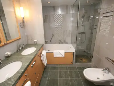 Ein helles, modern gefliestes Badezimmer an Bord der Oasis of the Seas. Zu sehen sind ein Doppelwaschbecken mit Marmorplatte, eine Badewanne, eine Duschkabine aus Glas und ein Bidet.