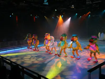 Eisshow an Bord der Oasis of the Seas: Darsteller in Entenkostümen gleiten auf einer bunten, hell beleuchteten Eisfläche mit Schlittschuhen.