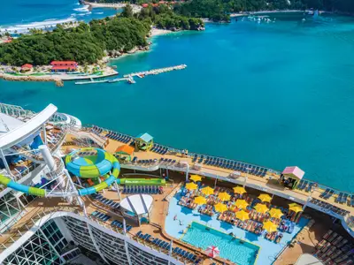 Blick auf die Oasis of the Seas mit Wasserpark und Pool. Dahinter tropische Insel mit Stränden und Meer.
