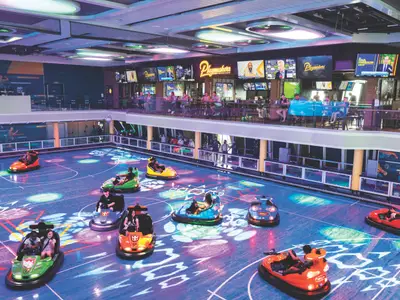 Bumper-Car-Arena mit aktiven Gästen auf der Odyssey of the Seas. Darüber die Sportsbar 'Playmakers' mit vielen Bildschirmen und Besuchern.
