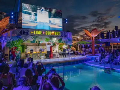 Abendveranstaltung auf dem Pooldeck der Odyssey of the Seas. Gäste sehen einer Show auf der Bühne mit großer LED-Leinwand zu. Beleuchteter Pool und Zuschauer mit Handys im Vordergrund.
