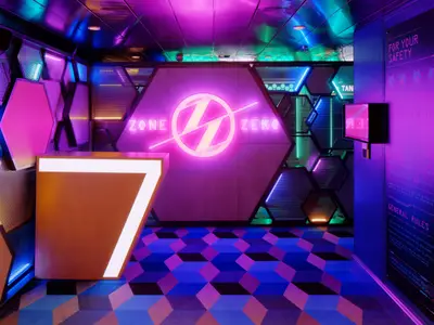 Eingangsbereich einer futuristischen Unterhaltungszone "ZONE ZERO" an Bord. Die Wände sind mit geometrischen Formen und Neonlichtern in Pink, Blau und Grün verziert. Ein orangefarbener Tresen steht im Vordergrund. Der Boden hat ein 3D-Kubusmuster.